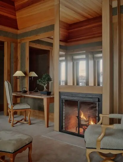 Suite at Aman Le Mélézin resort with fireplace, wooden ceiling and seating area.