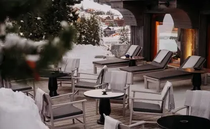 Terrasse enneigée d'Aman Le Mélézin avec sièges confortables et sapin décoré.