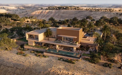 Aerial view of Amansamar's contemporary architecture set amongst palm trees in a desert landscape.