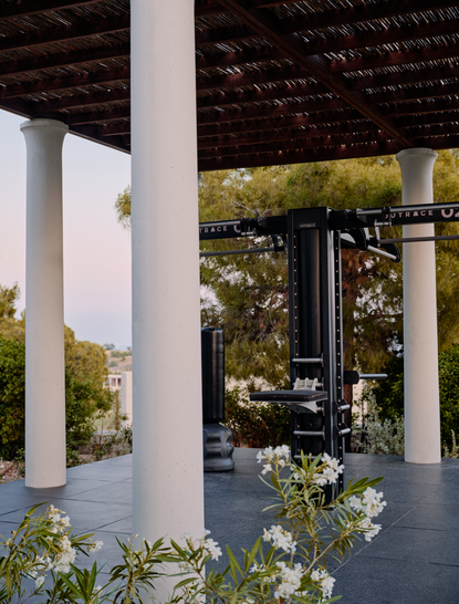 Outdoor gym space at Amanzoe resort in Greece, featuring white columns and exercise equipment beneath a covered structure surrounded by greenery.