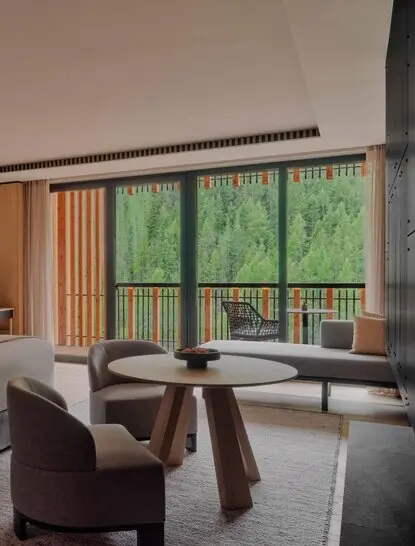 Junior Suite with floor-to-ceiling windows overlooking Alpine forest at Aman Rosa Alpina resort.