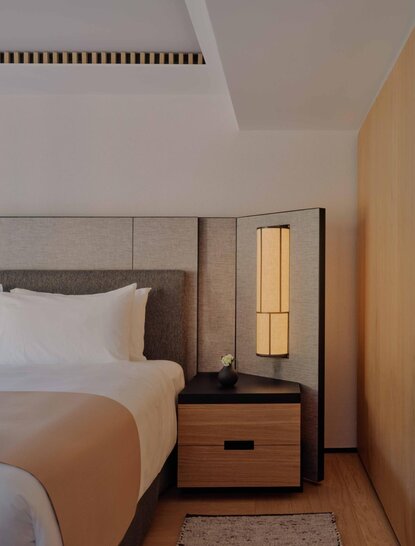 Premier Suite bedroom at Aman Rosa Alpina resort, with bed and wooden bedside table with lamp.