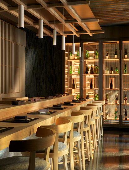 Dining venue at Aman New York com balcão de madeira clara, assentos altos e prateleiras iluminadas ao fundo.