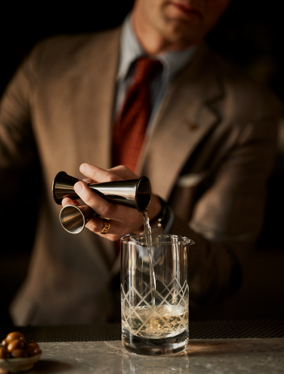 Bartender in tan suit pouring cocktail at Aman New York lounge bar.