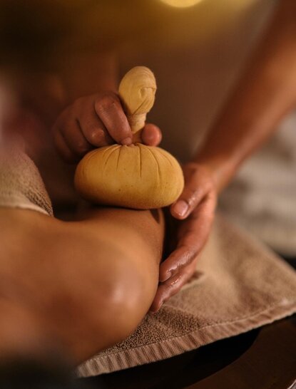 Therapist's hands holding a warm compress during a spa treatment at Amanbagh.
