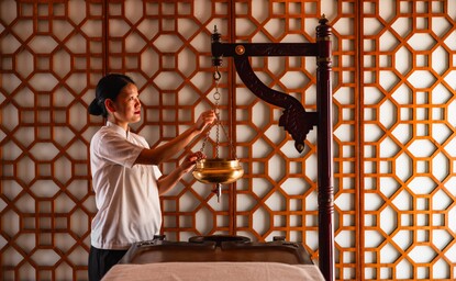 Therapist performing Shirodhara treatment at Amanbagh's spa, pouring warm oil over guest's forehead.