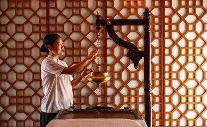 Therapist performing Shirodhara treatment at Amanbagh's spa, pouring warm oil over guest's forehead.