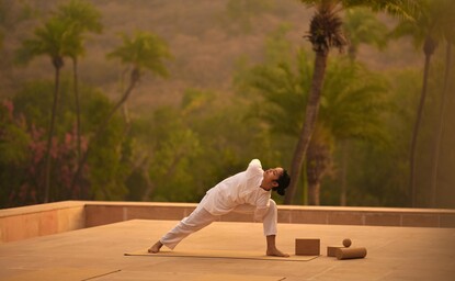 Yoga practice at Amanbagh's spa and wellness facility, with a guest in a forward bend pose on a wooden platform.