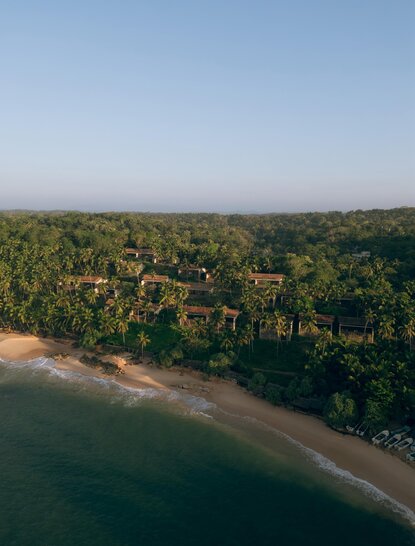 Aerial view of Amanwella's sandy beach cove bordered by dense tropical forest and calm turquoise waters.
