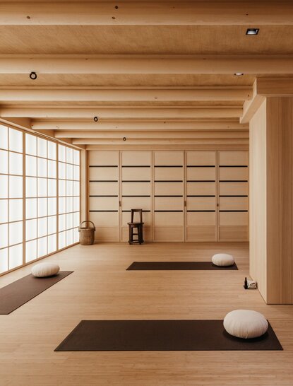 Yoga room at Aman Le Mélézin resort with wooden beams, natural light, and meditation props.