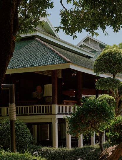 曼谷奈乐安缦酒店的传统泰式建筑外观，绿色倾斜屋顶和木制走廊围绕着树木。