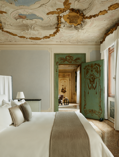 Alcova Tiepolo Suite principal bedroom at Aman Venice, with ornate frescoed ceiling and green doorway.