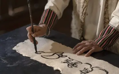 Hands demonstrating traditional Dongba calligraphy brushwork at Amandayan, China.