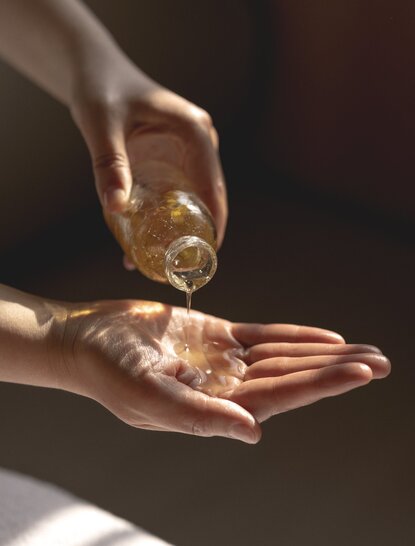 Therapist's hands pouring golden oil during a wellness treatment at Amandayan, China.