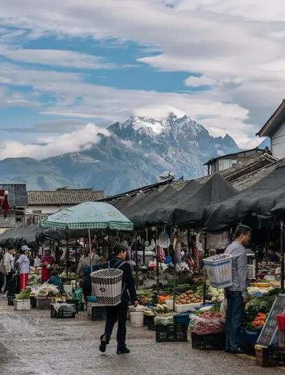 Vendors and visitors at Zhongyi Local Market in Amandayan, with snow-capped mountains beyond.