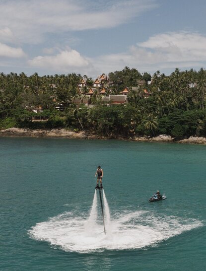 Person on flyboard above turquoise water at Amanpuri resort, Thailand.
