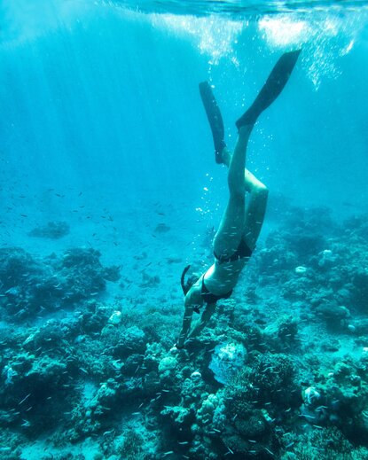 Diver descending towards coral reef in clear turquoise waters at Amanwana.
