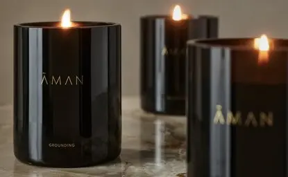 Trois bougies parfumées noires Aman Essentials avec flammes allumées, présentées à Amanyara resort.