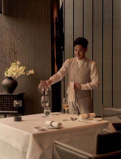Staff member pouring wine at a dining venue in Aman Nai Lert Bangkok, Thailand.