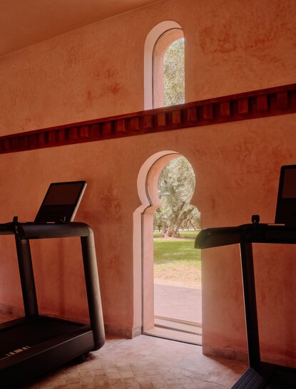 Amanjena gym with treadmills and arched doorways overlooking Moroccan gardens.