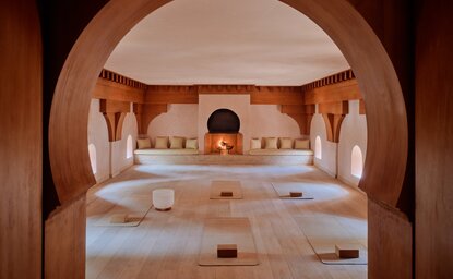 Amanjena's yoga studio with arched clay walls, cushioned mats, and candles creating a warm, contemplative space.