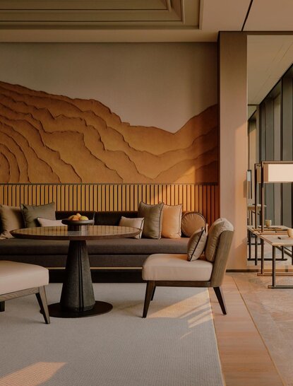 Premier Suite living area at Aman Nai Lert Bangkok, with curved wooden wall, seating arrangement and round table.