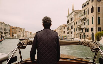 Man in dark jacket aboard Aman boat on Venice canal, Italy.