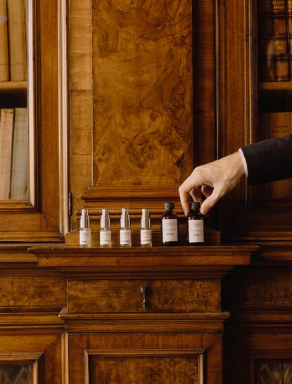 Hand reaching toward bottles on wooden shelf at Aman Venice perfume library.