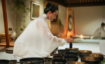 Woman in white robes playing singing bowl at Amanfayun, China.