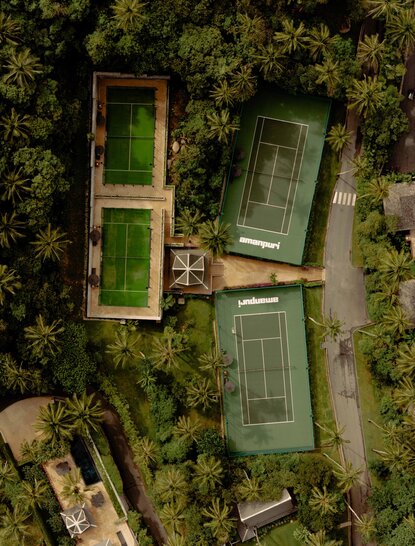 Aerial view of tennis courts at Amanpuri resort in Thailand, surrounded by lush vegetation.