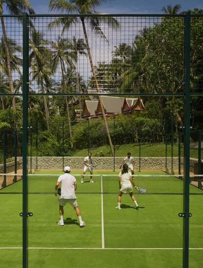 Padel court at Amanpuri resort in Thailand with players on the green court surrounded by tropical palms.