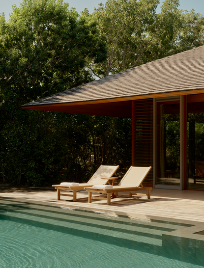 Pool pavilion at Amanyara with wooden loungers overlooking turquoise pool water and tropical greenery.