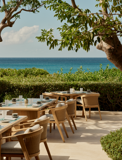 Breakfast dining area at Amanyara resort with wooden furniture overlooking turquoise waters and tropical coastline.