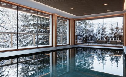 Indoor swimming pool at Aman Rosa Alpina with expansive windows overlooking snow-covered Italian Alpine landscape.