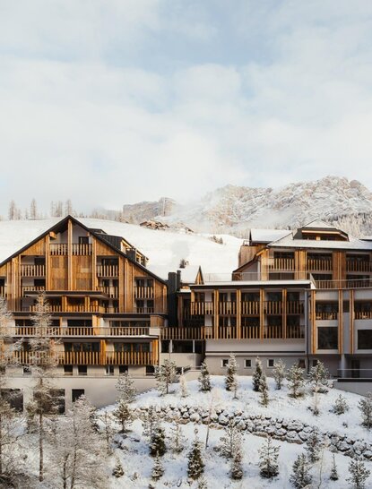 Aman Rosa Alpina exterior in winter, with snow-covered Dolomite peaks rising behind wooden chalets.