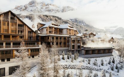 Aman Rosa Alpina exterior with snow-covered Alpine peaks rising behind traditional wooden architecture.