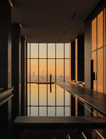 Wooden staircase descending towards floor-to-ceiling windows framing Tokyo's golden hour cityscape at Aman Tokyo.