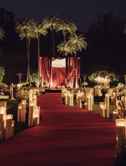 Red carpet wedding ceremony aisle lined with candles and palm trees at Amanbagh, India.