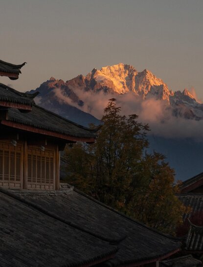 Golden sunrise light illuminates mountain peak above traditional rooflines at Amandayan.