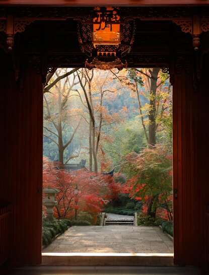 Autumn garden viewed through a wooden doorway at Amanfayun, with red foliage and stone pathway.