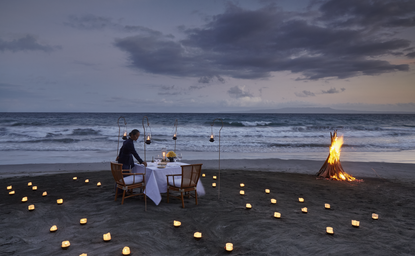 Couple dining by candlelight on a beach at Amankila resort, Indonesia, at dusk.