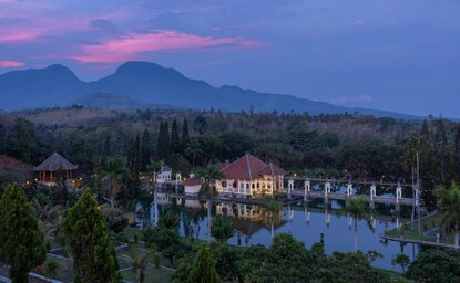 Amankila resort at dusk, with illuminated terraces reflected in pools and Mount Agung beyond, Karangasem, Bali.