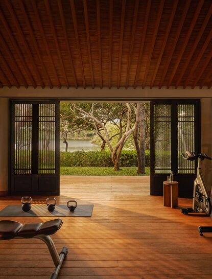 Amanoi resort's spa and wellness gym with wooden flooring, exercise equipment, and views of gardens through open glass doors.