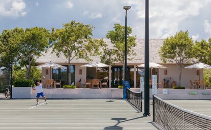Clubhouse tennis court at Amanyara resort with net, trees and pavilion structures in background.
