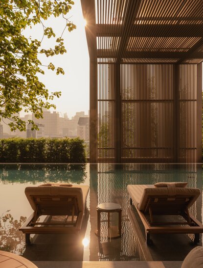 Wooden pavilion overlooking the pool at Aman Nai Lert Bangkok, with two leather chairs and river views beyond.