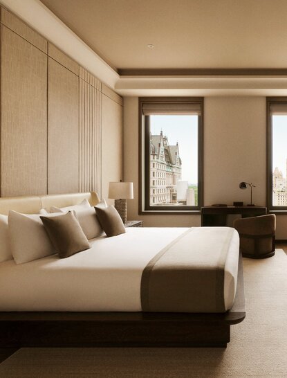 Principal bedroom at Aman New York with floor-to-ceiling windows, cream-upholstered bed, and warm neutral tones.