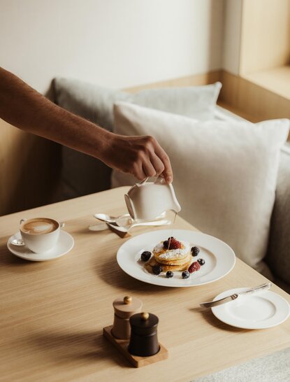 Person reaching for pastries at a wooden table in the Heritage Room at Aman Rosa Alpina.
