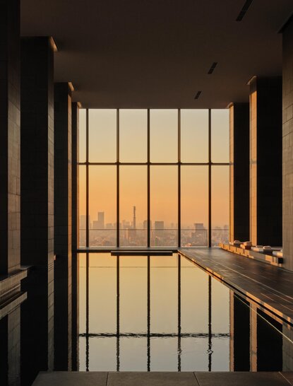 Wooden handrail overlooks floor-to-ceiling windows framing Tokyo's golden sunset at Aman Tokyo spa.