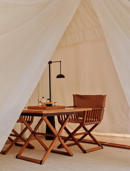Tented accommodation interior at Aman-i-Khas with wooden furniture and reading lamp beneath canvas ceiling.