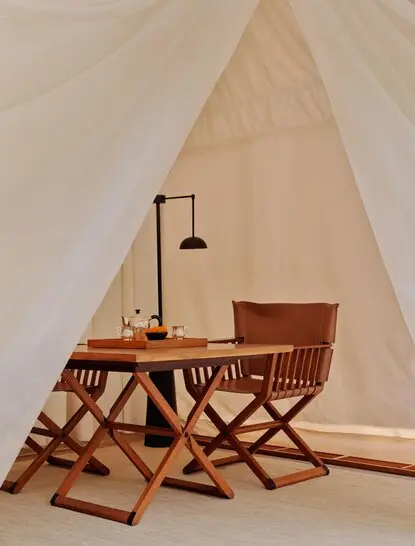 Tented accommodation interior at Aman-i-Khas with wooden furniture and reading lamp beneath canvas ceiling.